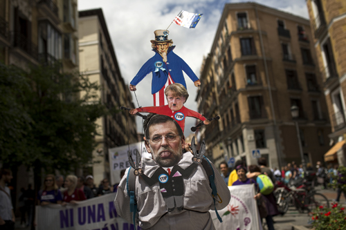 A man wears a banner against the Transatlantic Trade and Investment Partnership, with the images of the Spanish acting prime minister Mariano Rajoy (lower) and German Chancellor Angela Merkel, as he marches with others during a protest in Madrid, on Saturday (AP photo)